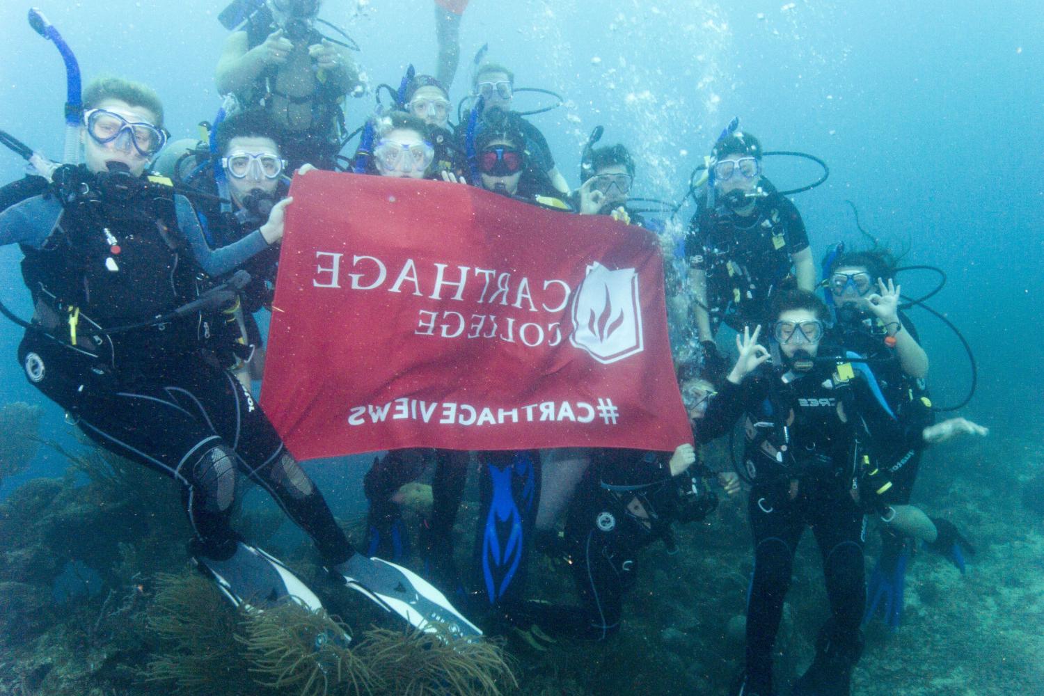 学生们手持<a href='http://hk34.hbwendu.org'>博彩网址大全</a>旗帜，在j学期洪都拉斯游学之旅中潜水.